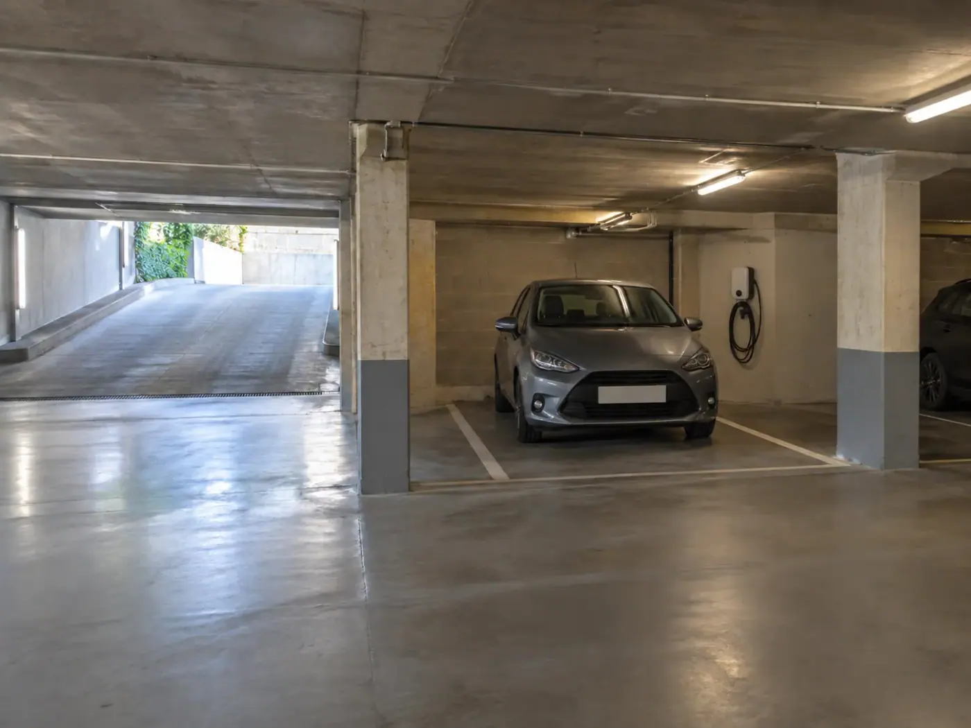 Place de stationnement entre deux piliers dans un parking souterrain avec rampe d’accès et borne de recharge