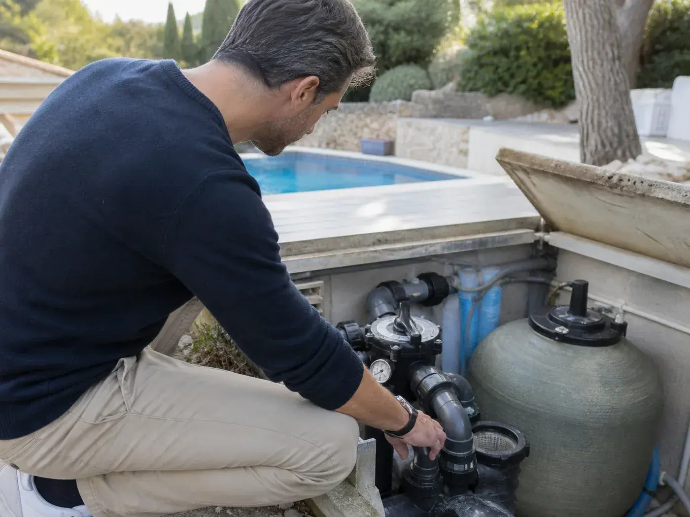 Personne examinant la pompe et le filtre d’une piscine dans un local technique extérieur