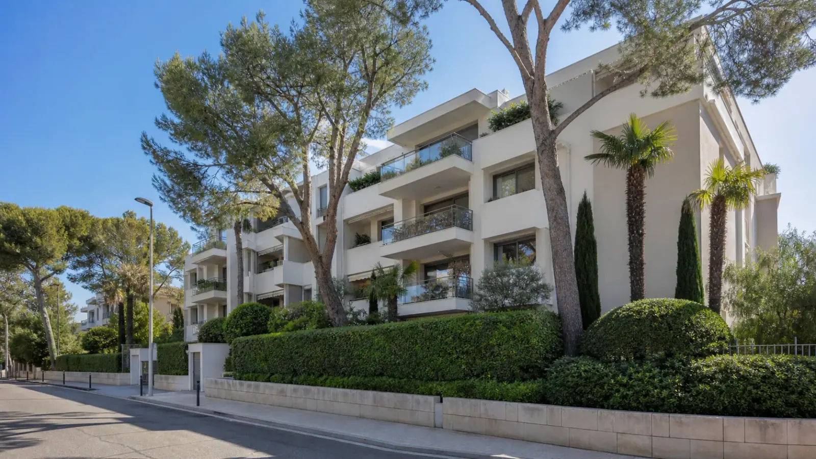 Immeuble résidentiel avec balcons entouré de pins et de palmiers sur la Côte d’Azur
