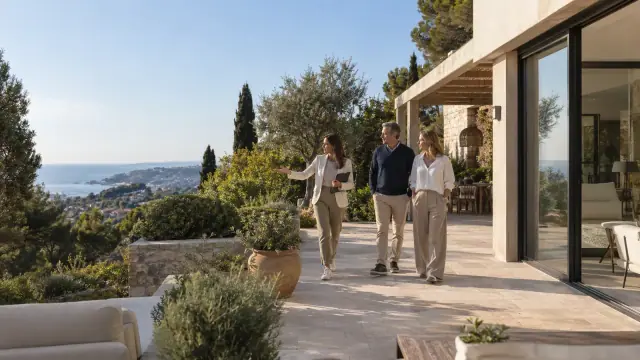 Trois adultes examinent une villa méditerranéenne sur une terrasse avec vue lointaine sur la mer